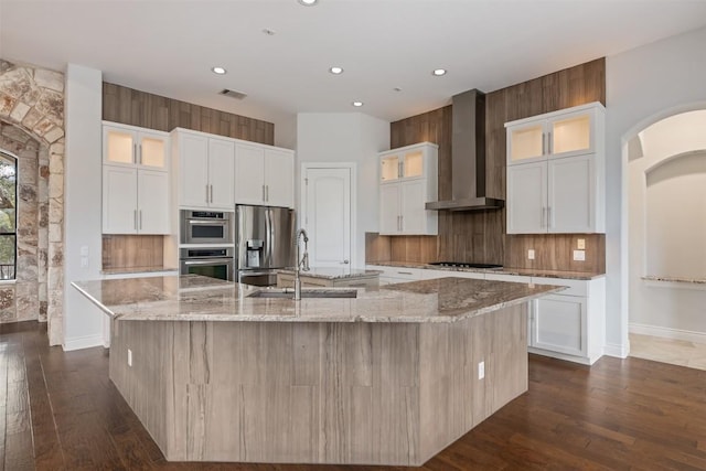 kitchen with visible vents, wall chimney range hood, a large island with sink, stainless steel appliances, and a sink