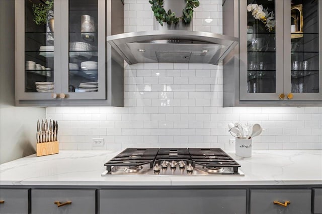 kitchen with decorative backsplash, gray cabinets, island exhaust hood, glass insert cabinets, and stainless steel gas cooktop