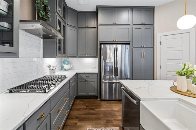 kitchen with gray cabinetry, stainless steel appliances, wall chimney range hood, decorative backsplash, and dark wood-style flooring