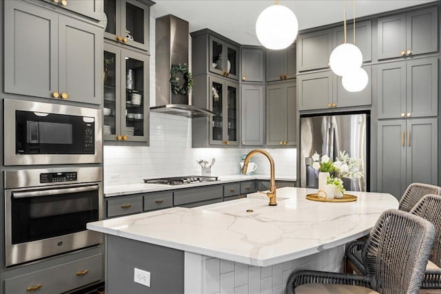 kitchen with gray cabinets, a sink, stainless steel appliances, wall chimney exhaust hood, and decorative backsplash