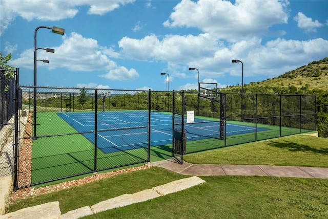 view of tennis court featuring community basketball court, fence, and a lawn