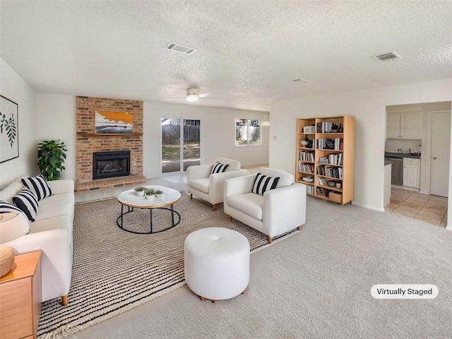 living area with a brick fireplace, light carpet, visible vents, and a textured ceiling