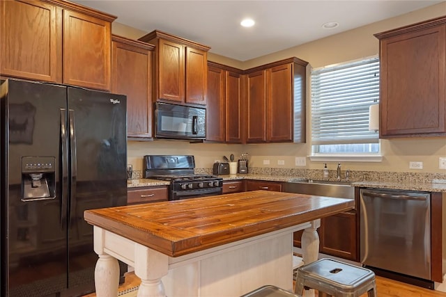 kitchen featuring butcher block counters, black appliances, a kitchen bar, and a sink