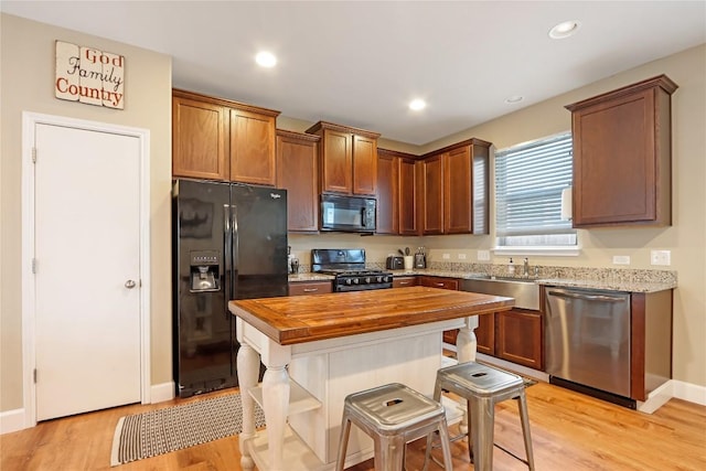 kitchen featuring light wood-style flooring, recessed lighting, a sink, black appliances, and butcher block counters