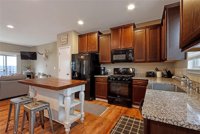 kitchen featuring light wood-style flooring, a sink, black appliances, a kitchen breakfast bar, and open floor plan