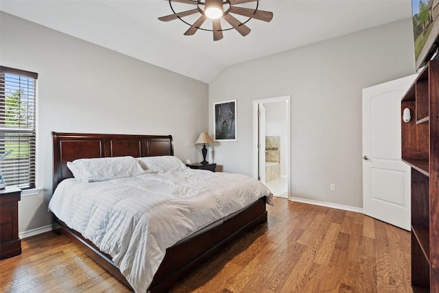 bedroom with a ceiling fan, wood finished floors, baseboards, ensuite bath, and vaulted ceiling