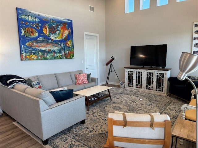 living area with visible vents, baseboards, wood finished floors, and a towering ceiling