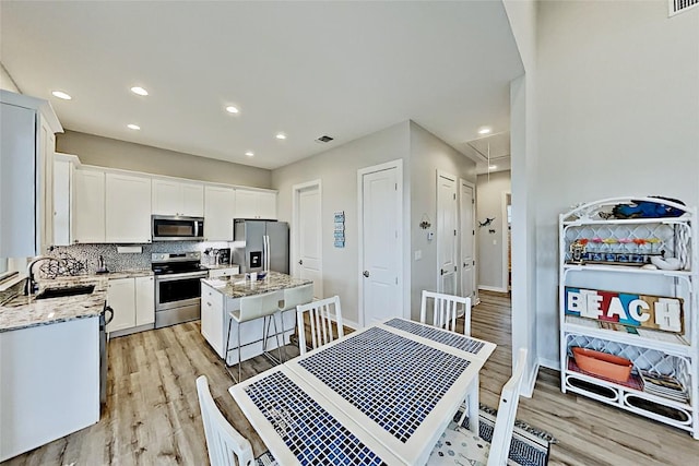 kitchen featuring a sink, a kitchen island, backsplash, stainless steel appliances, and light stone countertops