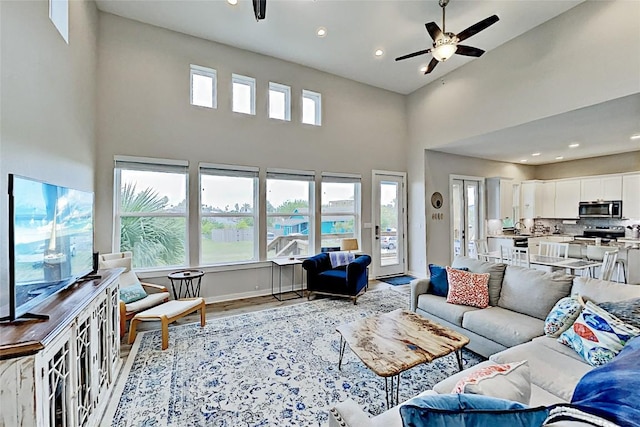 living area with baseboards, recessed lighting, a towering ceiling, wood finished floors, and a ceiling fan