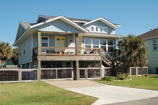 coastal home with a front lawn, fence, a standing seam roof, metal roof, and a ceiling fan