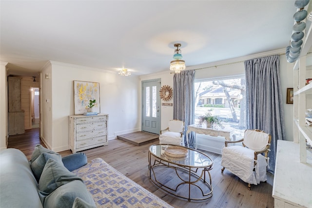 living room with an inviting chandelier, crown molding, baseboards, and wood finished floors