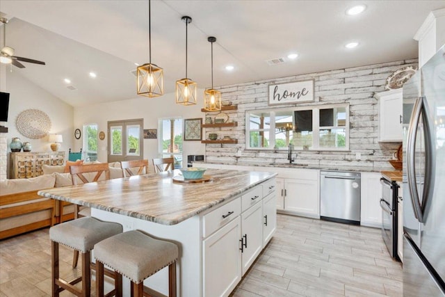 kitchen featuring visible vents, a sink, a kitchen breakfast bar, open floor plan, and appliances with stainless steel finishes