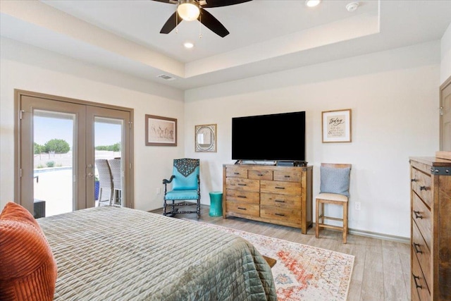 bedroom featuring french doors, a raised ceiling, light wood-style floors, and access to outside