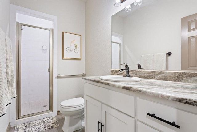 bathroom with vanity, toilet, wood finished floors, and a stall shower