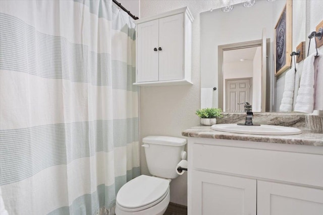 bathroom with toilet, vanity, and a textured wall