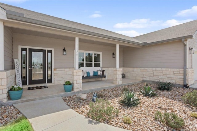 property entrance featuring stone siding, a porch, an attached garage, and a shingled roof