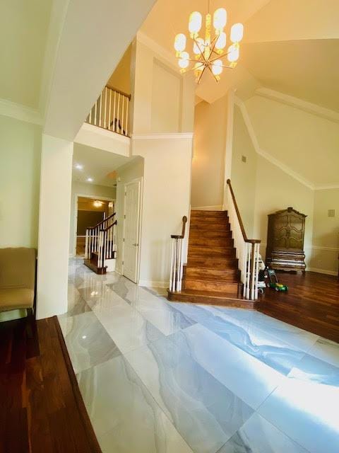 staircase with marble finish floor, baseboards, a notable chandelier, and high vaulted ceiling