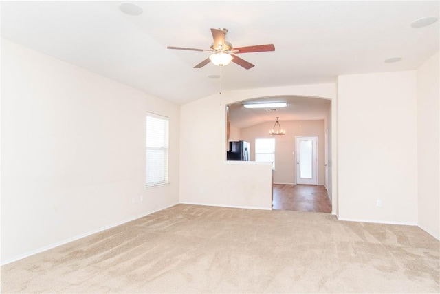 empty room with light carpet, plenty of natural light, arched walkways, and vaulted ceiling