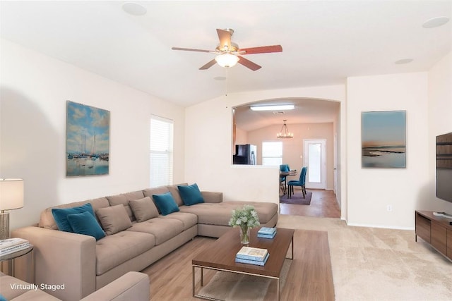 living room featuring ceiling fan with notable chandelier, lofted ceiling, light colored carpet, and arched walkways