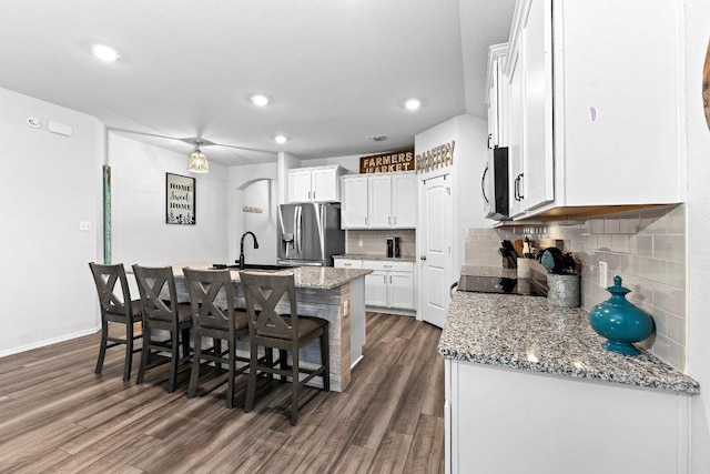 kitchen featuring a kitchen bar, dark wood finished floors, stainless steel appliances, and an island with sink