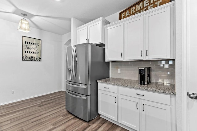 kitchen with light stone counters, wood finished floors, white cabinets, stainless steel refrigerator with ice dispenser, and tasteful backsplash