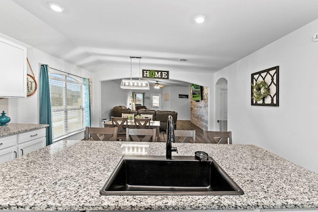 kitchen with a sink, white cabinetry, arched walkways, light stone countertops, and vaulted ceiling