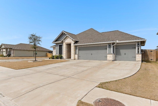 view of front of house featuring fence, roof with shingles, a garage, stone siding, and driveway