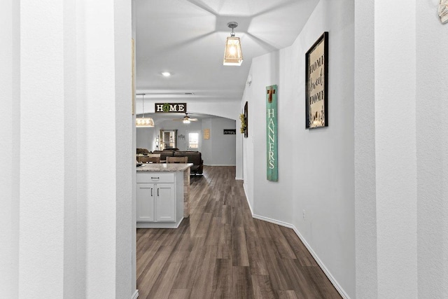 corridor featuring dark wood-type flooring, baseboards, and arched walkways