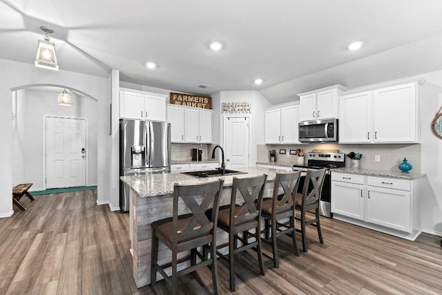 kitchen with dark wood-type flooring, a center island with sink, white cabinets, stainless steel appliances, and a sink