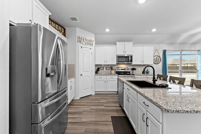 kitchen featuring visible vents, dark wood finished floors, stainless steel appliances, white cabinetry, and a sink