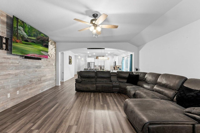 living room featuring a ceiling fan, dark wood-style floors, arched walkways, vaulted ceiling, and wood walls