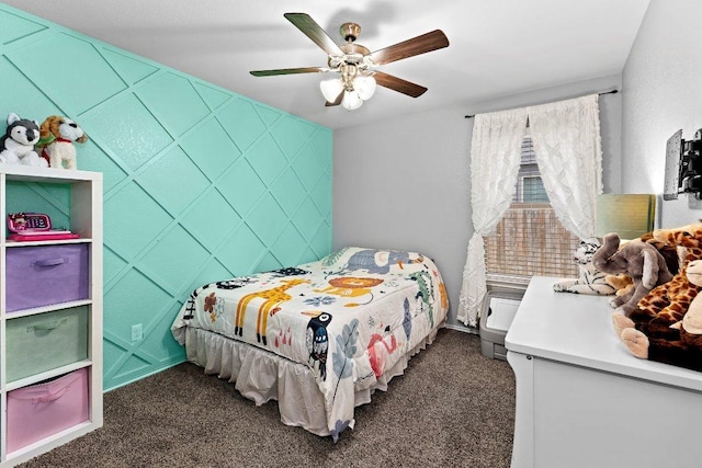 bedroom featuring an accent wall, a ceiling fan, and dark colored carpet