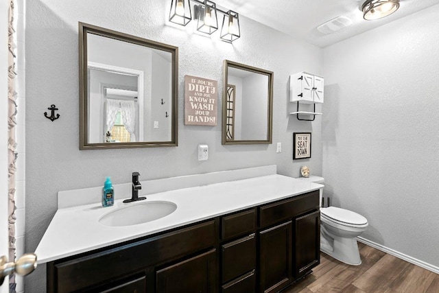 bathroom featuring vanity, wood finished floors, visible vents, toilet, and a textured wall