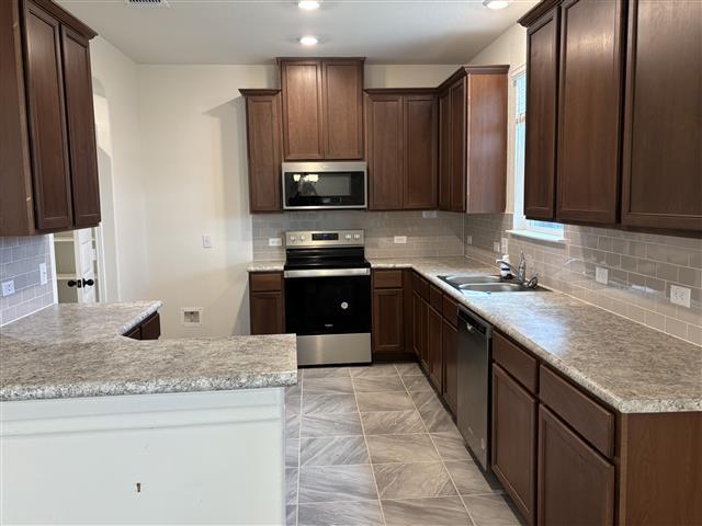 kitchen featuring a sink, stainless steel appliances, a peninsula, light countertops, and decorative backsplash