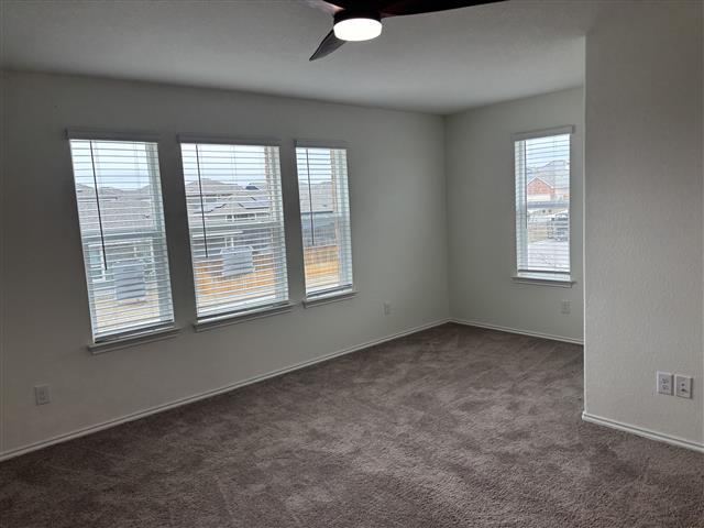 spare room with dark colored carpet, baseboards, and ceiling fan