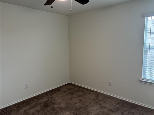 empty room featuring dark carpet, baseboards, and ceiling fan