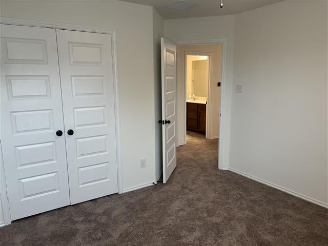 unfurnished bedroom with baseboards, a closet, and dark carpet