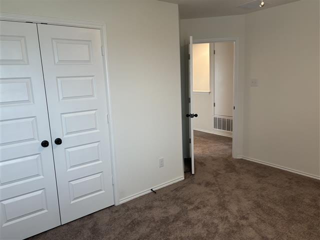 unfurnished bedroom with a closet, visible vents, dark carpet, and baseboards