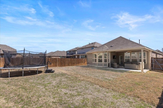 rear view of house with a hot tub, a trampoline, a lawn, a fenced backyard, and a patio area