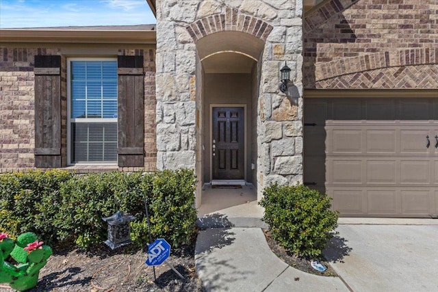 view of exterior entry with a garage, stone siding, and brick siding