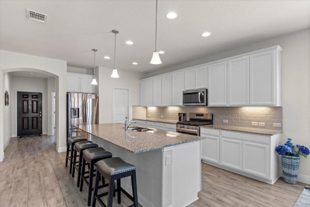 kitchen featuring visible vents, backsplash, arched walkways, stainless steel appliances, and a sink