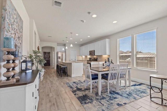 dining space with visible vents, arched walkways, light wood finished floors, and baseboards