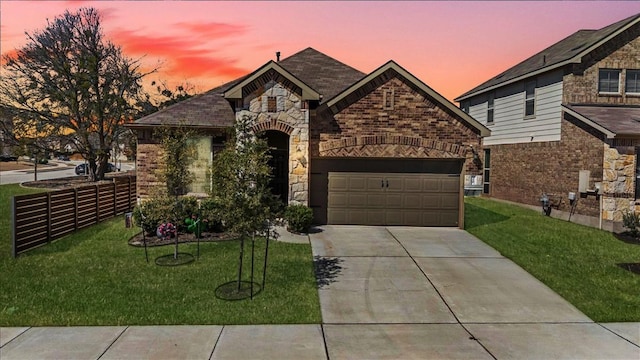 french country inspired facade featuring stone siding, a lawn, concrete driveway, and an attached garage