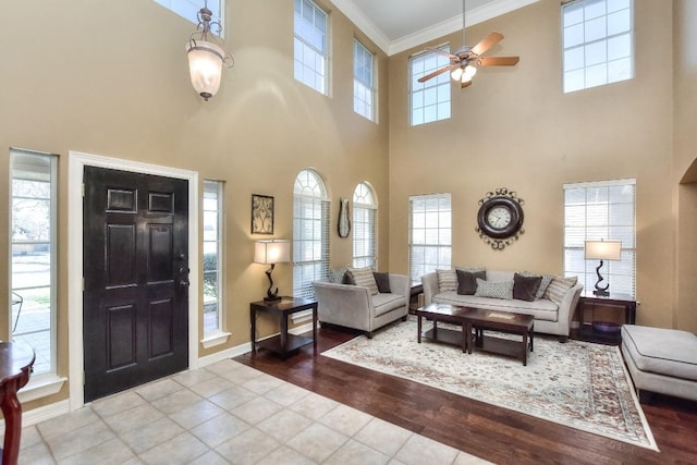 tiled living room with baseboards, ornamental molding, and a ceiling fan