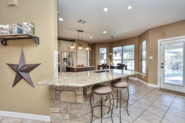 kitchen with visible vents, a breakfast bar, stainless steel fridge with ice dispenser, a sink, and a center island