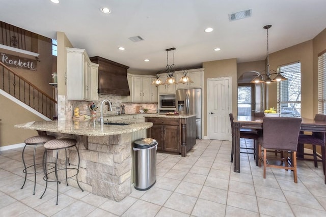 kitchen featuring a notable chandelier, a sink, backsplash, stainless steel appliances, and a peninsula