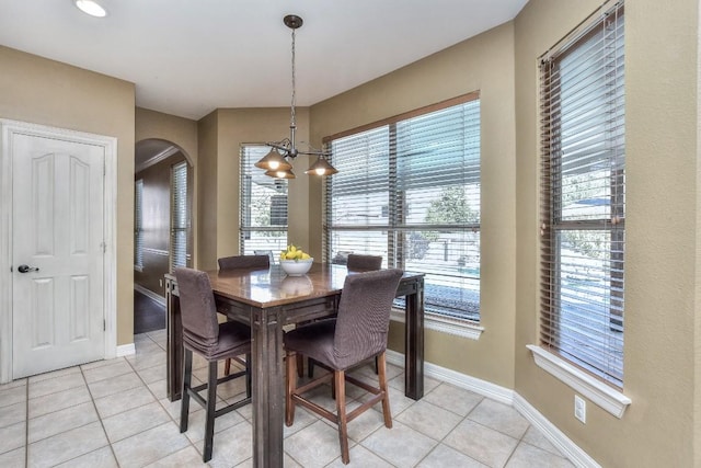 dining room with a notable chandelier, light tile patterned flooring, baseboards, and arched walkways