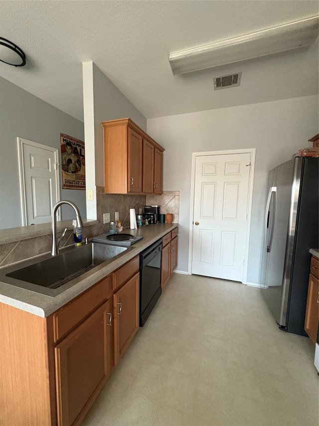 kitchen featuring visible vents, black dishwasher, freestanding refrigerator, brown cabinetry, and a sink