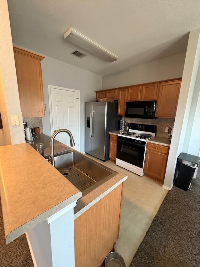 kitchen featuring visible vents, a sink, black microwave, range with gas cooktop, and stainless steel fridge