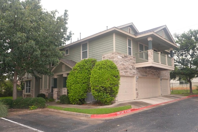 view of side of home with a garage, stone siding, a balcony, and fence